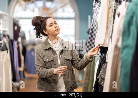 Side view of young pretty Caucasian woman choices clothes in shop. Concept of black friday. Stock Photo