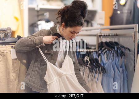 Caucasian young woman choices dress in shop. Concept of consumerism. Stock Photo