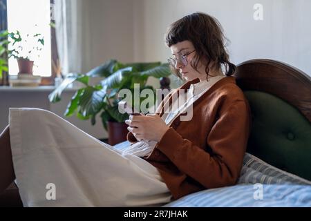 Focused pensive teenage girl using mobile phone scrolling on social media while relaxing at home Stock Photo