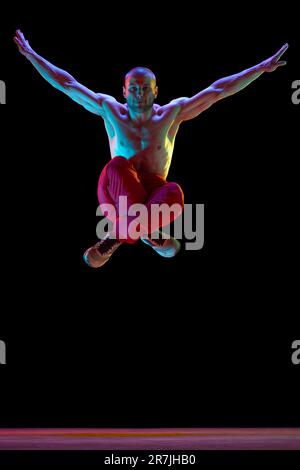 Freedom of movements. Young muscular guy, street dancer performing, dancing breakdance against black studio background in neon light Stock Photo