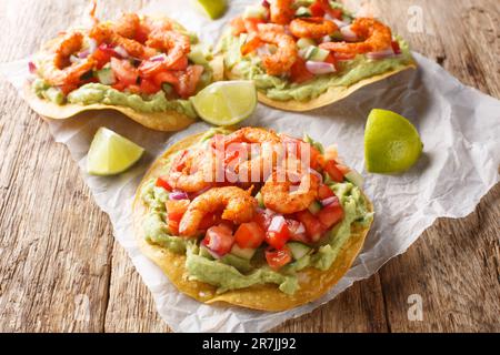 Crispy tostadas topped with guacamole, spiced shrimp, and fresh salsa closeup on the wooden table. Horizontal Stock Photo