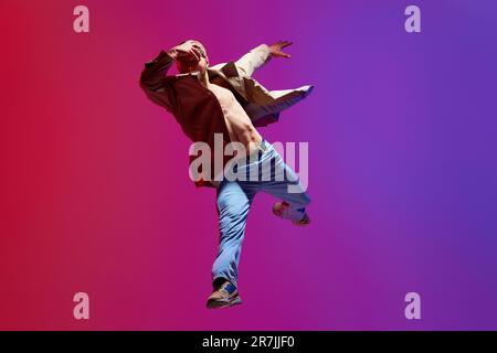 Active, artistic young man in casual clothes dancing breakdance, contempt against pink purple studio background Stock Photo