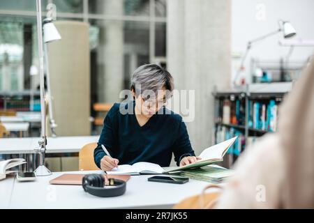Asian student writing in notebook at table in library Stock Photo