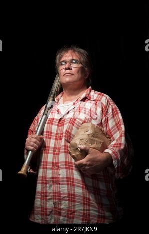 A middle aged Canadian man wearing a plaid shirt carries his baseball bat and lunch while standing in a studio built on the sidewalk on the corner of Broadview Avenue and Gerrard S Stock Photo
