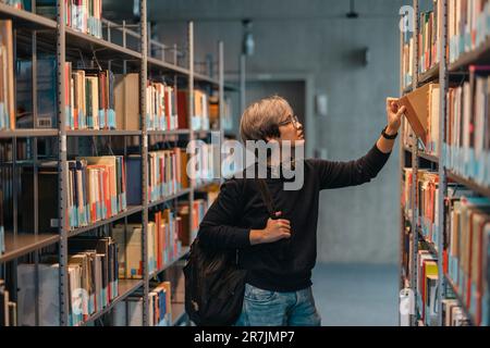 Portrait of asian student picking book from bookshelf in library Stock Photo