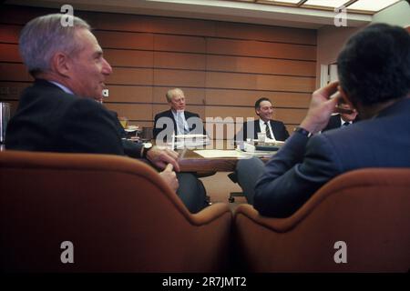 Employees of a large financial company conduct a light-hearted meeting around a large conference table in a corporate office. Stock Photo