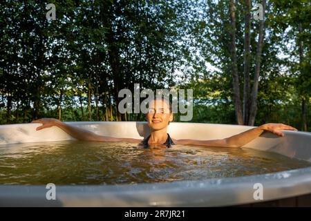 woman relaxing and enjoying outdoor hot tub at sunset in forest. nature spa Stock Photo