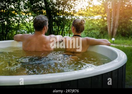 young couple relaxing together in outdoor hot tub at forest resort. spa nature treatment, romantic getaway Stock Photo