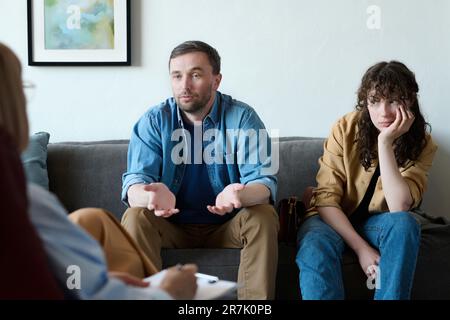 Young man talking to psychologist about problems with his wife during session in office Stock Photo