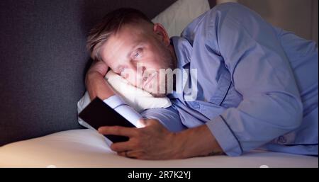 Man Lying On Bed Using Mobile Phone At Night Stock Photo
