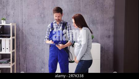Young Male Pest Control Worker Showing Invoice To Woman In Domestic Kitchen Stock Photo