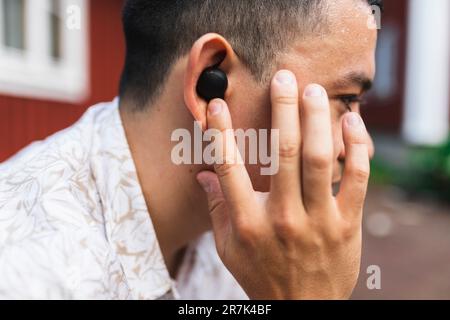 Young man adjusting in-ear headphones Stock Photo