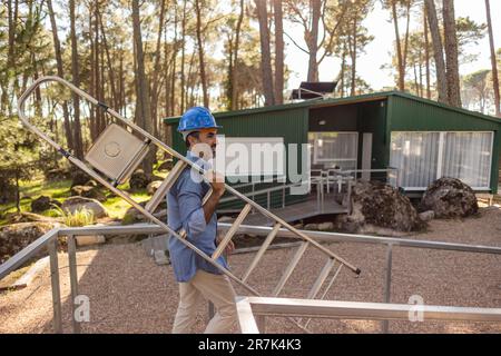 Construction worker carrying ladder wearing hard hat Stock Photo