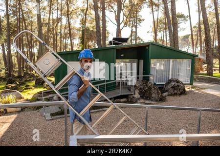 Construction worker carrying ladder wearing hard hat Stock Photo - Alamy