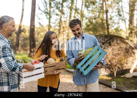 Friends carrying vegetable crates looking smiling at freshly harvested produce Stock Photo