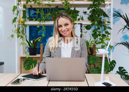 Smiling young businesswoman using laptop and digital tablet at desk Stock Photo
