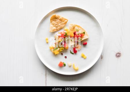 Yellow corn tortilla chips topped with homemade salsa on a white plate. Stock Photo