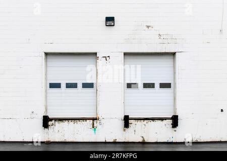 Front view of a truck loading bay with rubber bumpers in the white concrete wall of a warehouse with a closed white roller shutter door Stock Photo