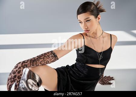 spring fashion photography, elegant asian woman with bold makeup, in black strap dress, silver accessories and animal print gloves sitting on grey bac Stock Photo - Alamy spring fashion photography, elegant asian woman with bold makeup, in black strap dress, silver accessories and animal print gloves sitting on grey bac Stock Photo - Alamy