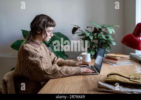 Teen girl using laptop at home taking online courses to develop new skills Stock Photo