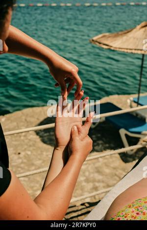 On a sunny day, on a seaside beach, a female masseur massages the palm and fingers of a young girl's right hand Stock Photo