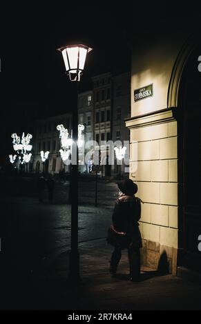 A mature adult female standing outdoors near a street lamp wearing a long coat in Stolarska street Stock Photo