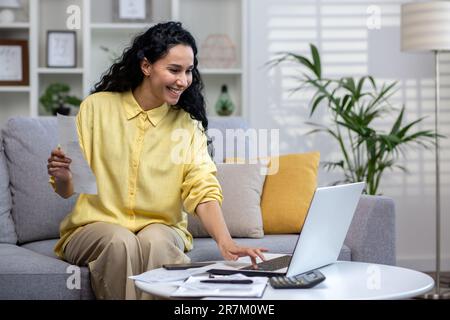 Smiling young beautiful woman reading banking paper notification about last mortgage payment while calculating budget at home. Happy hispanic girl feeling excited of good news in letter notice Stock Photo