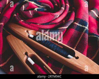 Two boat shuttles and handwoven fabric in red and black colors, close up. Ready weaving project, selective focus Stock Photo