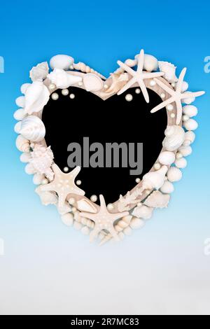 Heart shape seashell and oyster pearl wooden frame on gradient blue and white background with chalkboard. Abstract summer sea life nature border. Stock Photo