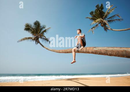 Man sitting on trunk of palm tree and enjoying sea view. Idyliic sand beach in Sri Lanka. Stock Photo