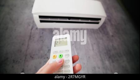 Close-up Of Person's Hand Holding Remote In Front Of Air Conditioner Stock Photo