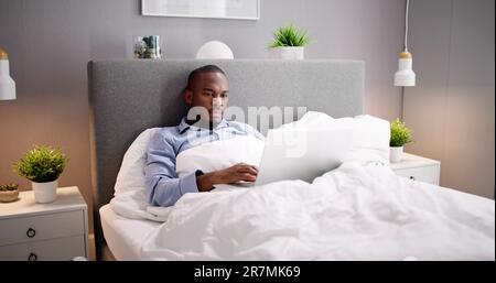 Happy Man Sitting On Bed Using Laptop Stock Photo