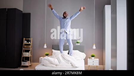 Happy Excited African Man Jumping On Bed At Home Stock Photo