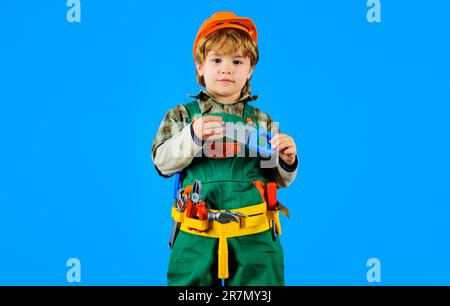 Little child boy in builder uniform and safety helmet with saw. Little boy in hardhat with toy tools set. Little repairman or construction worker in t Stock Photo