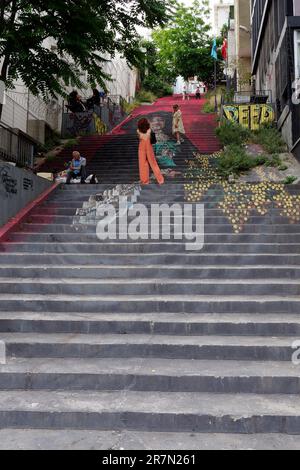 Woman in orange outfit stands on painted steep steps in the evening in the Karakoy district of Istanbul, Turkey Stock Photo