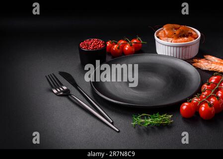 Ingredients for cooking cherry tomatoes, shrimp, salt and spices with a place for an inscription on a dark concrete background Stock Photo