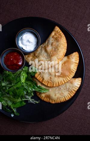 top view fried chebureks with sauce and herbs on a black plate Stock Photo