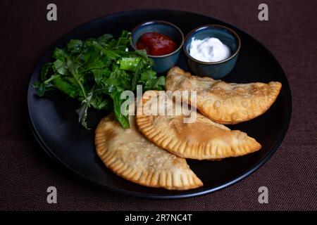 fried chebureks with sauce and herbs on a black plate Stock Photo