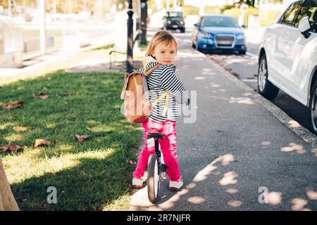 Outdoor portrait of a cute little toddler girl, riding a bike, wearing backpack Stock Photo