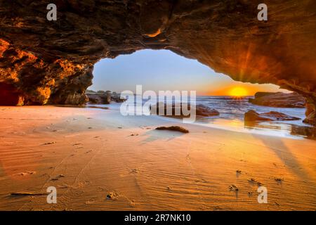 Bright rising sun shining to sea cave on Pacific coast of Australia at Caves beach. Stock Photo