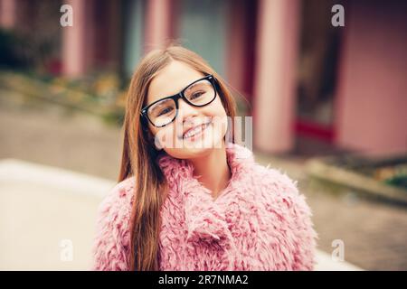 Outdoor portrait of cute young kid girl wearing eyeglasses and pink coat Stock Photo