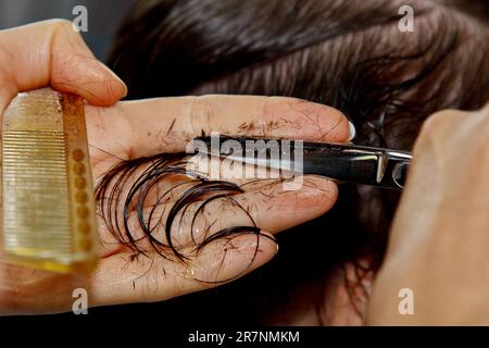 Closeup of a hairdresser cuts the wet brown hair of a client in a salon. Hairdresser cuts a woman. Side view of a hand cutting hair with scissors Stock Photo