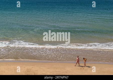 Two young Caucasian girls walking in bikinis along the sand, on the shore of the Mediterranean Sea in the town of Salou, Tarragona, Catalonia, Spain. Stock Photo