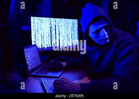 Hacker in mask working with computers in dark room. Cyber attack Stock Photo