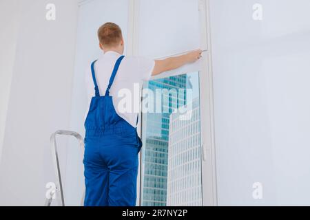 Worker installing roller window blind on stepladder indoors Stock Photo