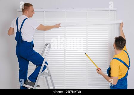 Workers in uniforms installing horizontal window blinds indoors Stock Photo