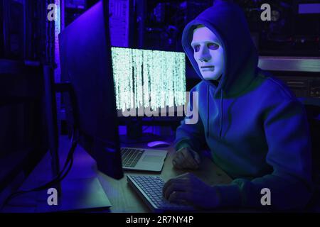 Hacker in mask working with computers in dark room. Cyber attack Stock Photo