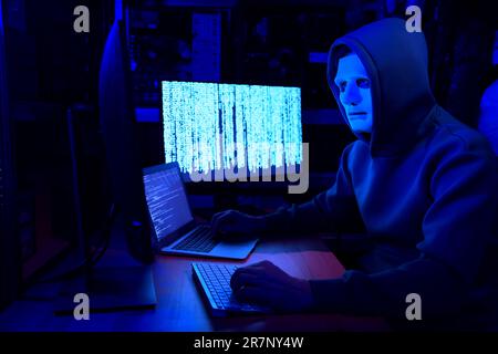 Hacker in mask working with computers in dark room. Cyber attack Stock Photo