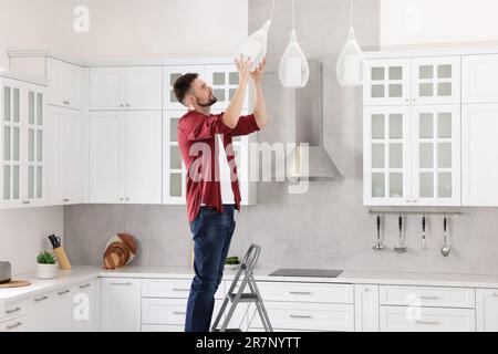 Young man installing ceiling lamp on stepladder in kitchen Stock Photo