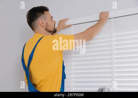 Worker in uniform installing horizontal window blinds indoors Stock Photo